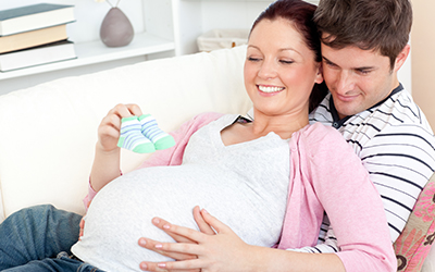 Happy pregnant woman holding baby shoes