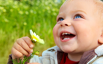 A baby smiling with a flower in his hand