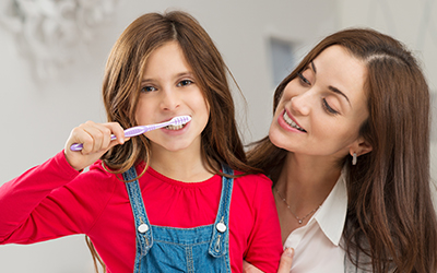 A young girl with her mother brushing her teeth