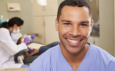 A dentist smiling with other dental assistants in the back