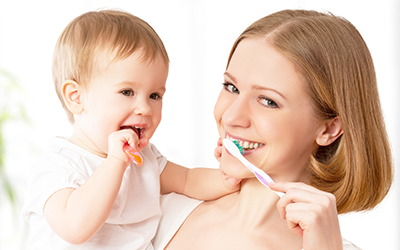 A mom and her baby brushing their teeth together