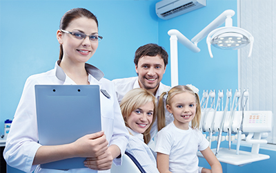 A dentist smiling with a young child and parent