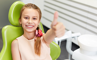 Young happy girl showing a thumbs up gesture at a dental clinic